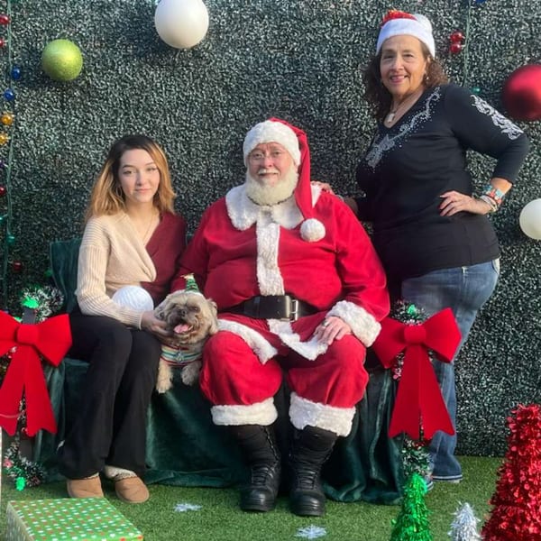 Santa Claus, a woman, and a dog in a festive setting with a green wall and ornaments.