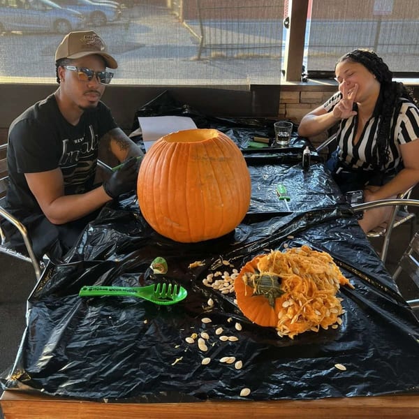 Two people carving pumpkins at a table covered with a black tarp at Wolfies Sports Bar.