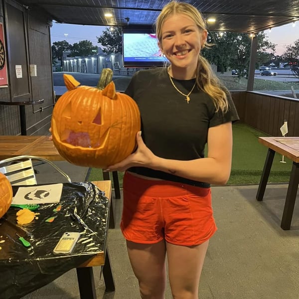 A smiling woman holds a carved pumpkin with cat ears at Wolfies Restaurant and Sports Bar.