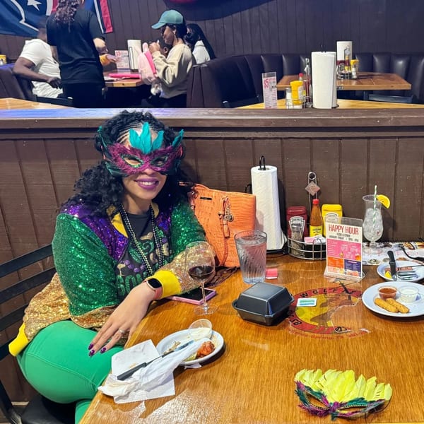 A woman in a Mardi Gras mask and sequined jacket sits at a table in Wolfies Sports Bar.