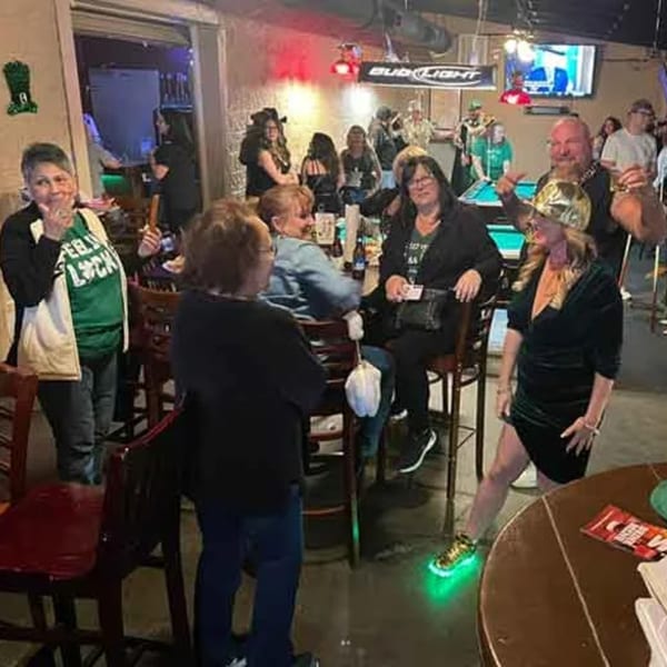 Patrons enjoying drinks and conversation in a lively sports bar, with a pool table in the background.