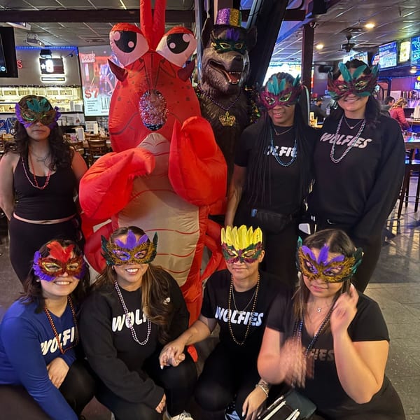 Wolfies staff in Mardi Gras masks and beads pose with a giant lobster and wolf mascot.