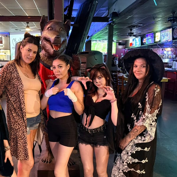 Four women in Halloween costumes pose with a wolf statue inside Wolfies Sports Bar.