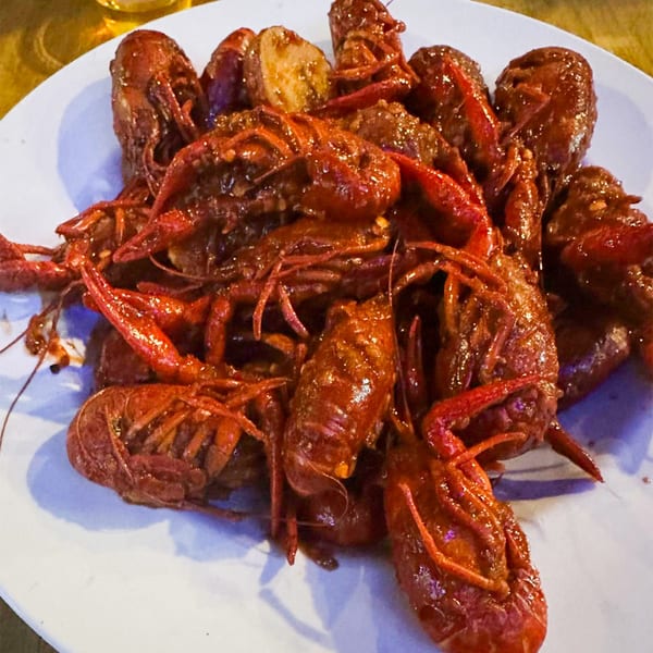 A white plate piled high with red, cooked crawfish and potatoes, glistening with sauce.