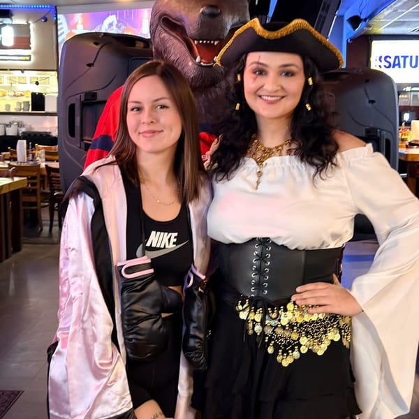 Two women in costumes, one a boxer and one a pirate, posing in a sports bar.