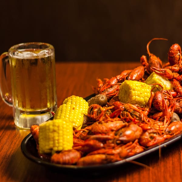 A plate of crawfish boil with corn on the cob and potatoes, next to a mug of beer.