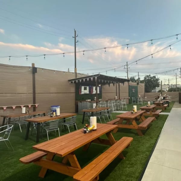 Outdoor patio at Wolfies Sports Bar with picnic tables on artificial turf under string lights.