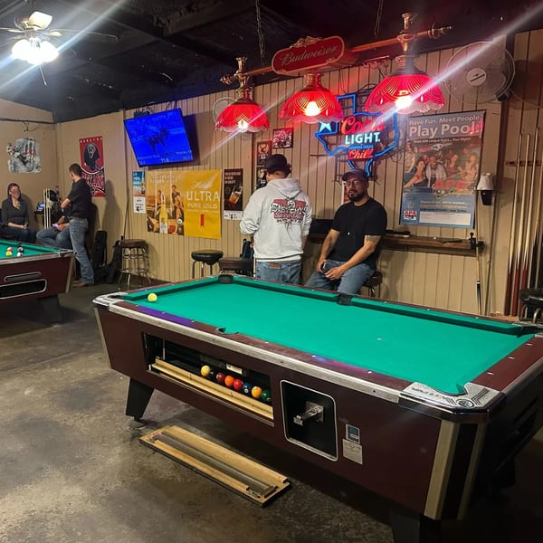 Patrons play pool at Wolfies Sports Bar, with neon signs and sports memorabilia adorning the walls.