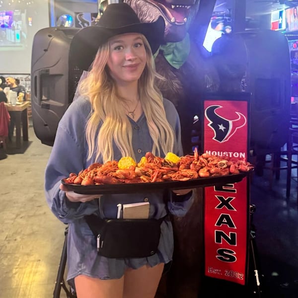 A woman in a cowboy hat holds a large tray of crawfish and corn at Wolfies Sports Bar.