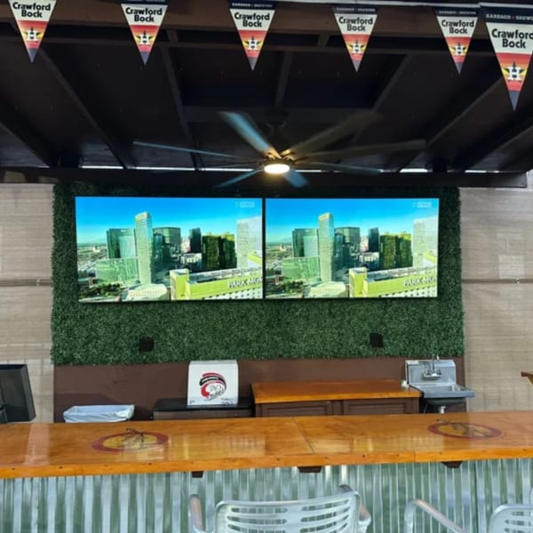 A sports bar interior with a wooden bar, two large screens displaying a city, and "Crawford Bock" banners.