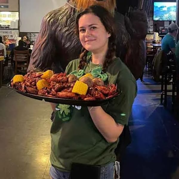 A server at Wolfies Sports Bar holds a large tray of crawfish, corn, and potatoes.