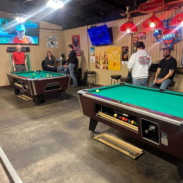 Patrons play pool at Wolfies Sports Bar, with TVs showing sports and neon signs illuminating the room.