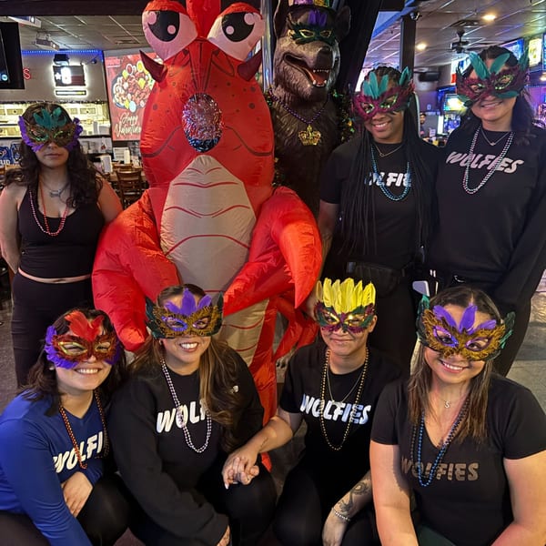 Wolfies staff in Mardi Gras masks and beads pose with a red inflatable lobster and a wolf statue.