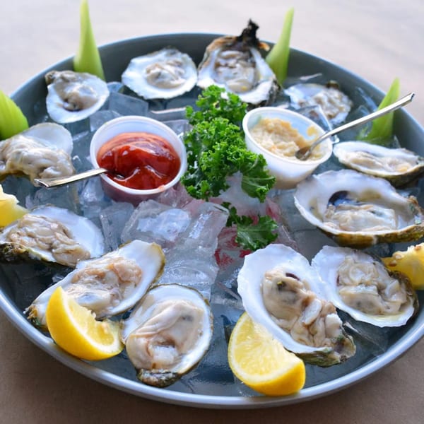 A platter of fresh oysters on ice with lemon wedges, cocktail sauce, and horseradish.