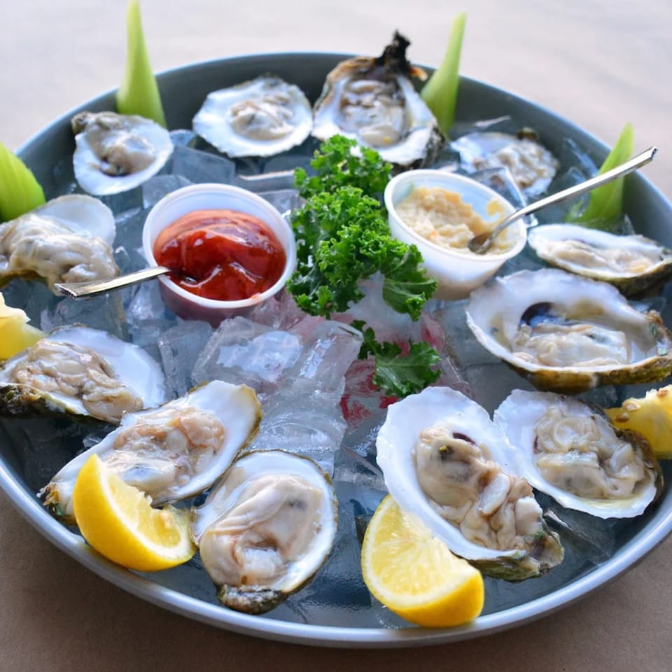 A platter of fresh oysters on ice with lemon wedges, cocktail sauce, and horseradish.