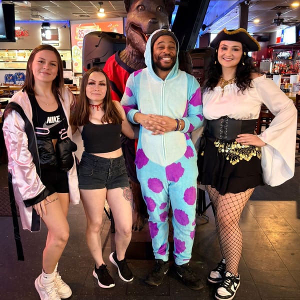 Four people in Halloween costumes, including a boxer, devil, Sully, and pirate, pose at Wolfies.