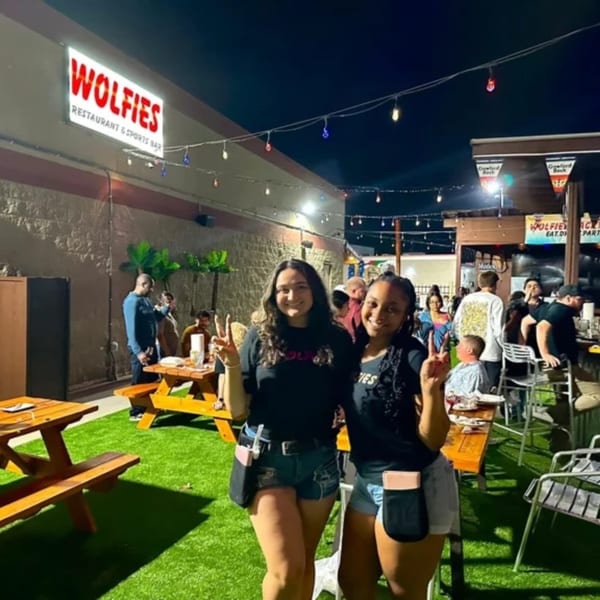 Two women pose with peace signs on Wolfies Restaurant & Sports Bar's outdoor patio at night.