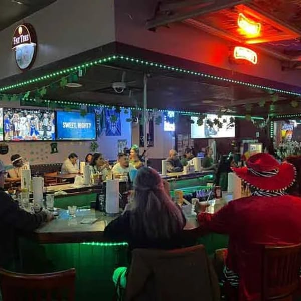Wolfies sports bar with patrons at the counter, green lighting, and multiple TVs showing sports.