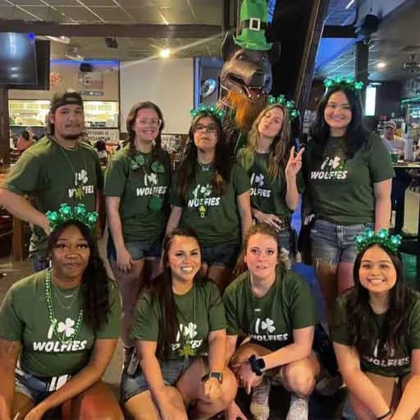 Wolfies staff in green shirts and St. Patrick's Day headbands pose with a wolf statue.