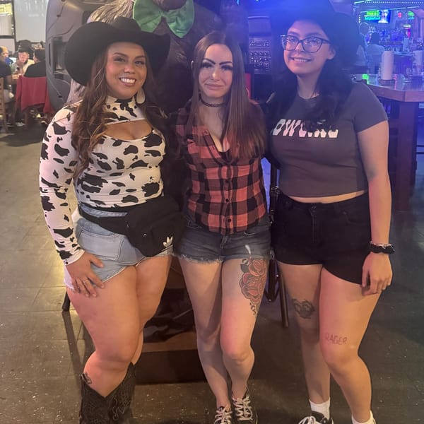 Three women in cowboy hats and casual attire pose together inside Wolfies sports bar.