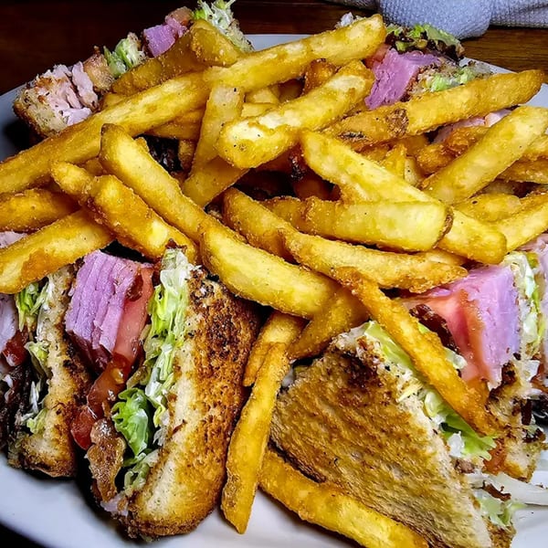 A close-up of a large club sandwich with fries, featuring toasted bread, lettuce, and purple meat.