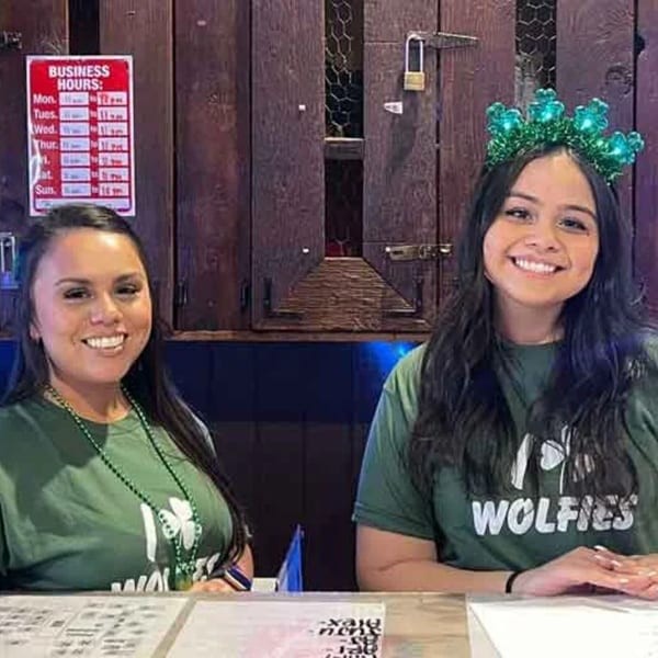 Two smiling Wolfies staff members in green shirts, one wearing a shamrock headband.