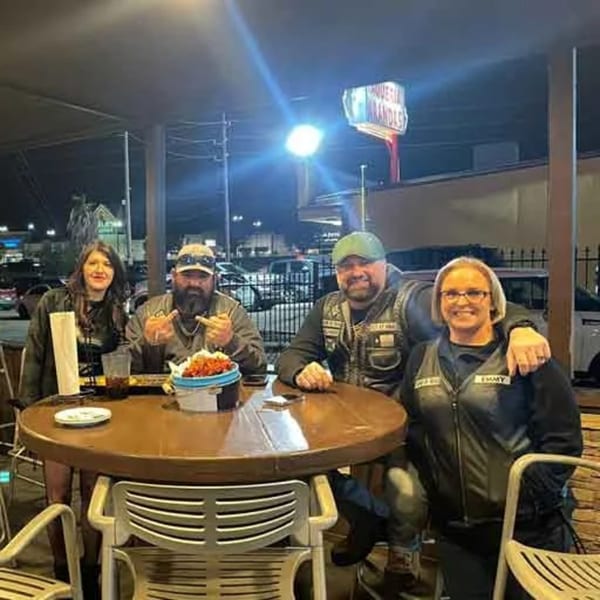 Four patrons enjoying drinks and food at a high-top table on Wolfies Restaurant's outdoor patio at night.