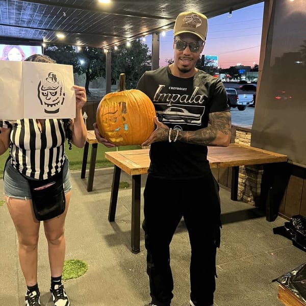 Two people on a patio holding a carved pumpkin and a Frankenstein monster stencil.