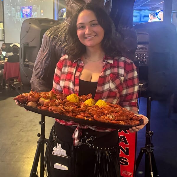 Smiling server in a plaid shirt holding a large tray of crawfish and corn at Wolfies.