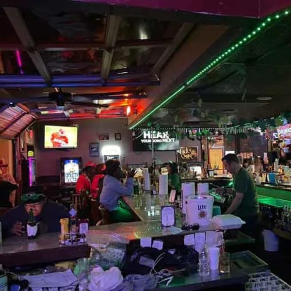 Patrons and a bartender at a lively sports bar with green and red neon lighting.