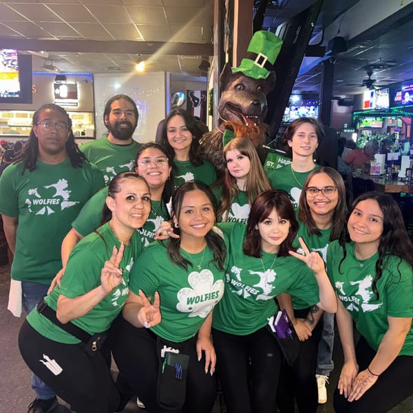 Wolfies Restaurant and Sports Bar staff in green shirts pose with a wolf mascot wearing a leprechaun hat.