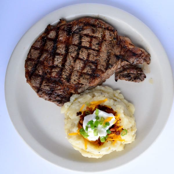 Grilled steak with mashed potatoes topped with cheese, bacon, sour cream, and chives.