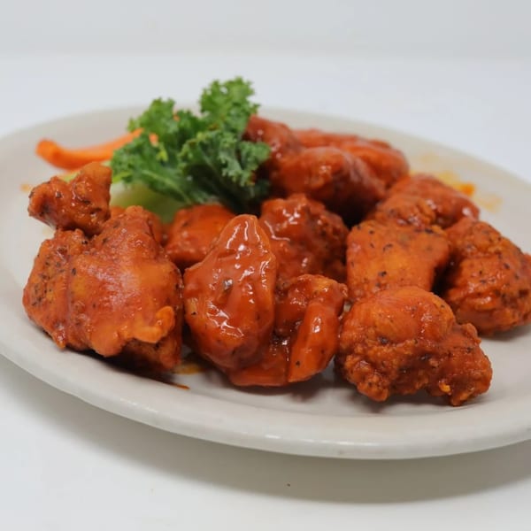 A plate of Wolfies boneless wings coated in red sauce, garnished with kale and carrots.