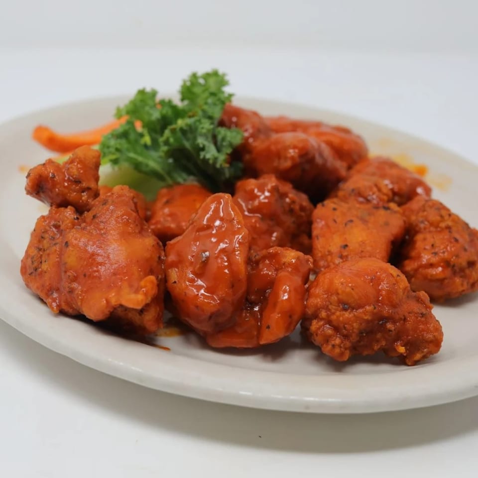 A plate of Wolfies boneless wings coated in red sauce, garnished with kale and carrots.