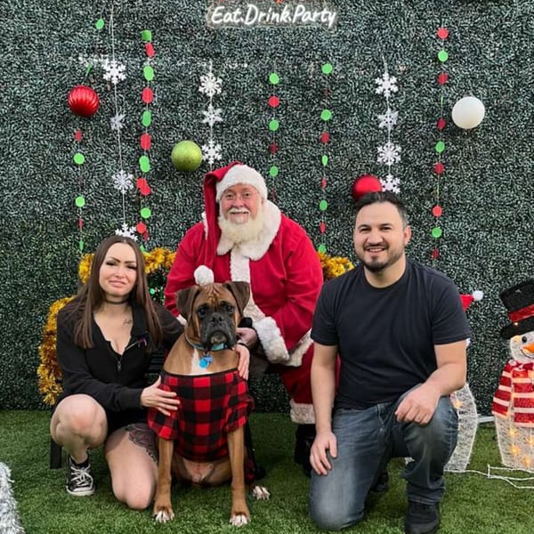 A woman, Santa, and a man pose with a dog in a festive Christmas setting at Wolfies Sports Bar.