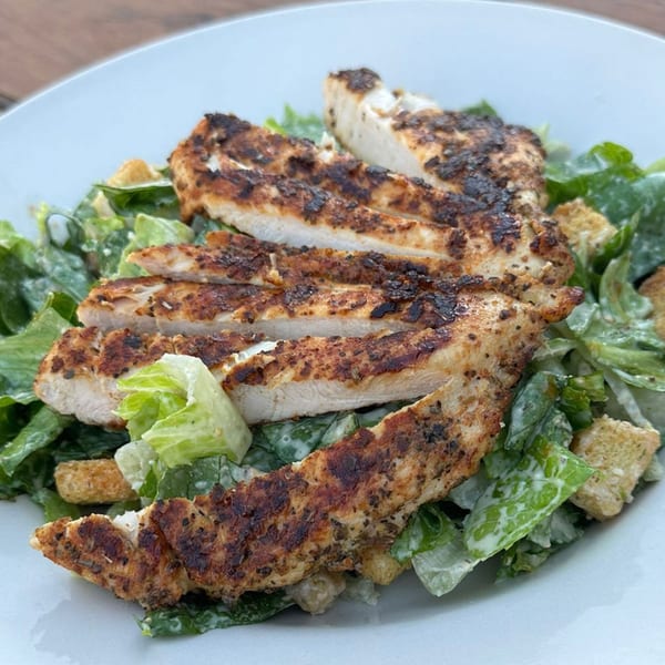 Grilled chicken Caesar salad with croutons and dressing on a white plate at Wolfies Sports Bar.