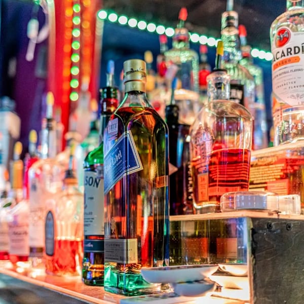 Close-up of liquor bottles on a bar shelf, illuminated by colorful lights at Wolfies Sports Bar.